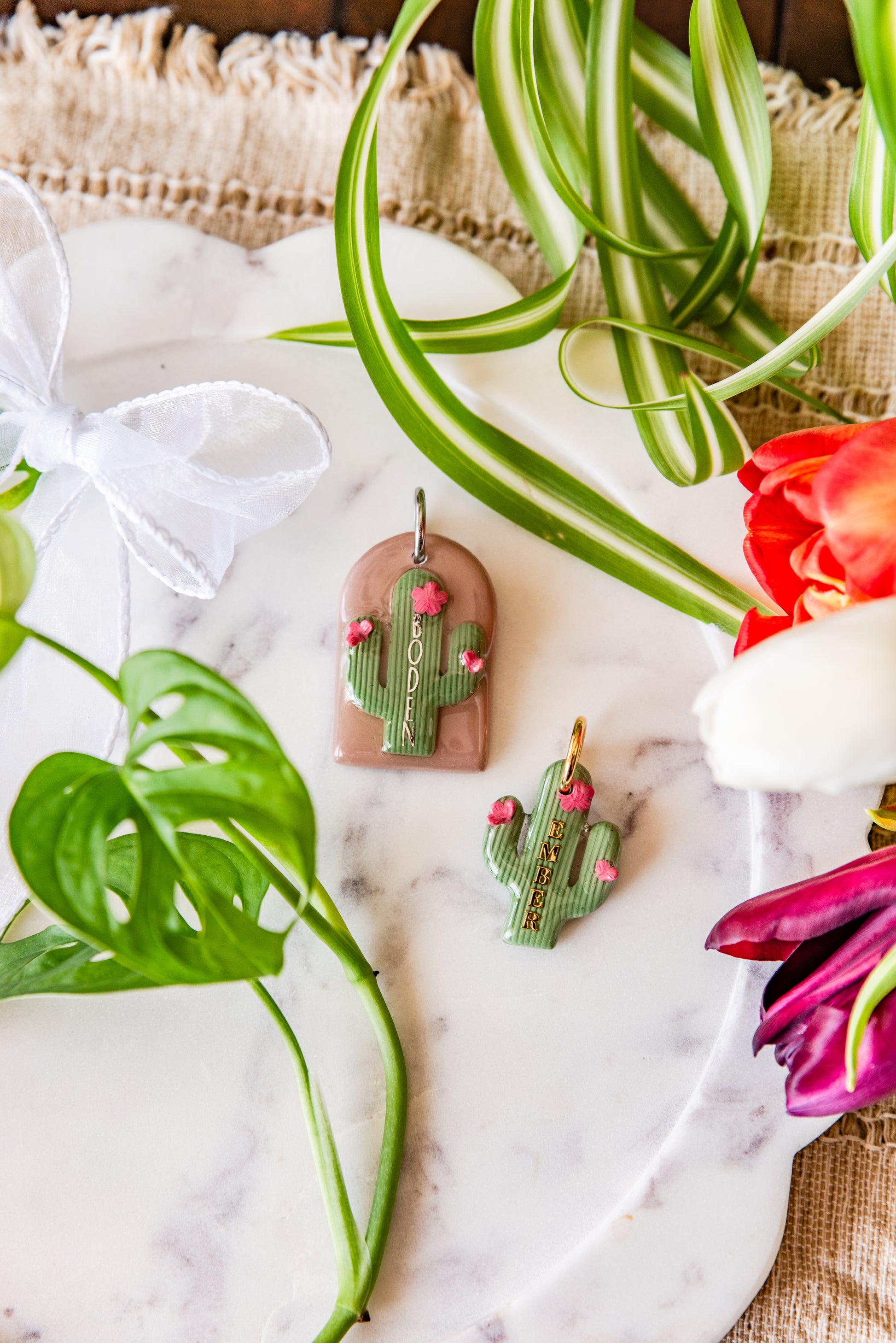 Cactus-shaped pet tags on a marble surface with plants and flowers.