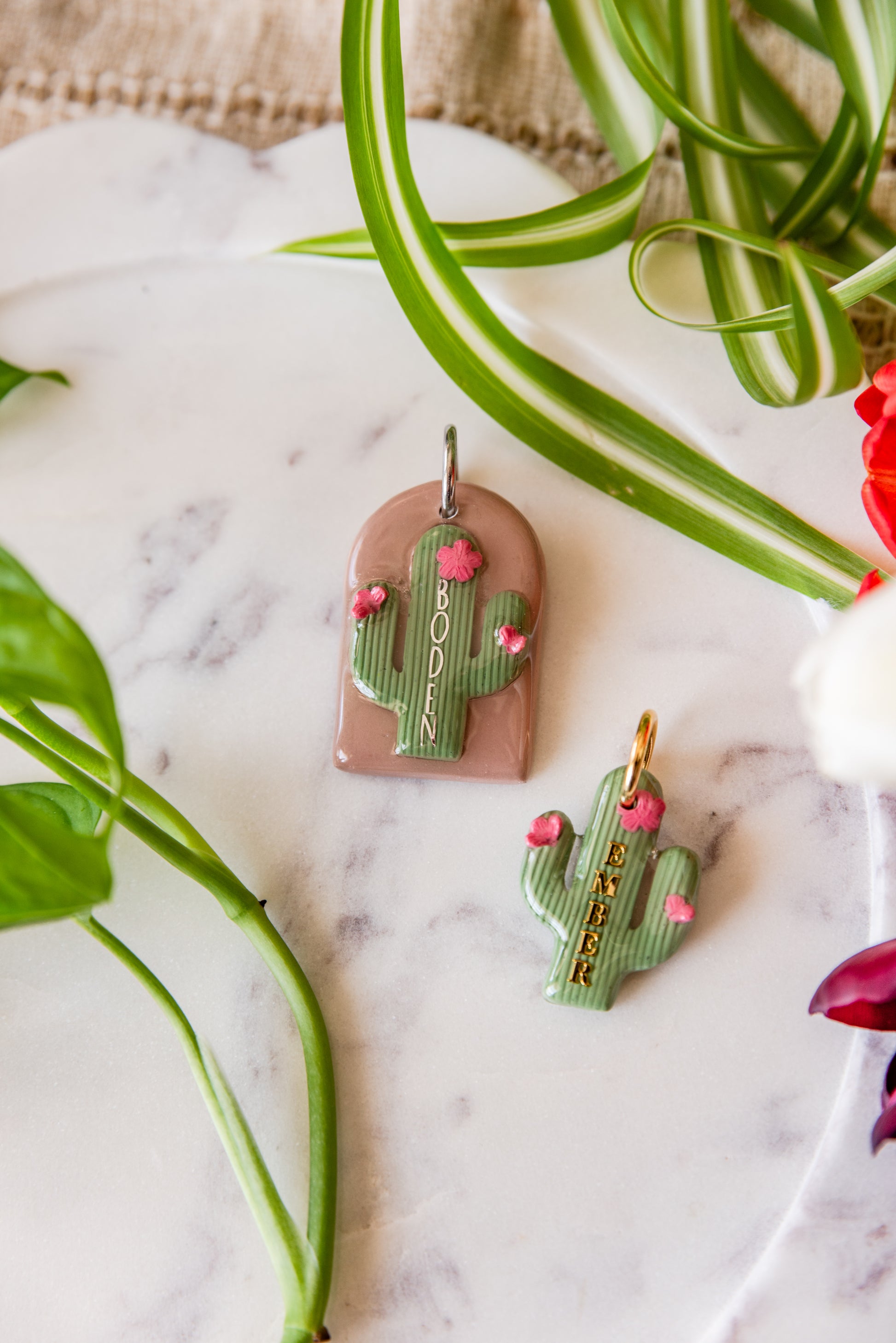 Cactus-themed pet tags on a marble surface with plants in the background